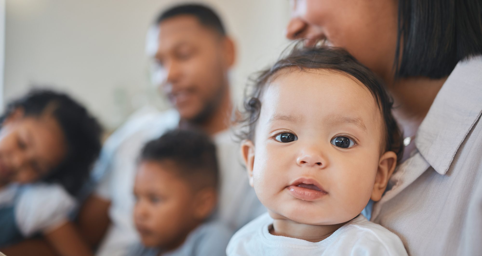 A baby looking at the camera with family behind